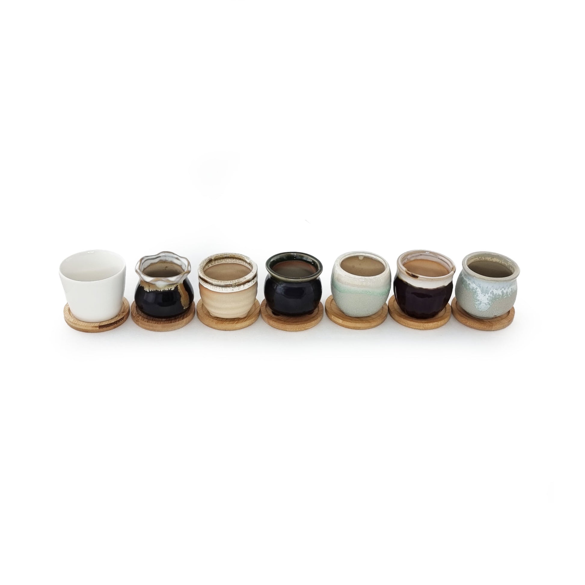 1 white and 6 different glaze painted pots styles with bamboo drip trays side by side